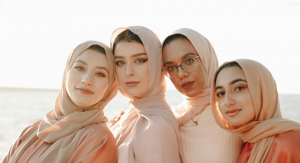 Four young women in hijabs enjoying a sunny day by the water, embracing togetherness and friendship.